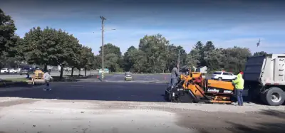 Paver, crew and haul truck on a commercial lot